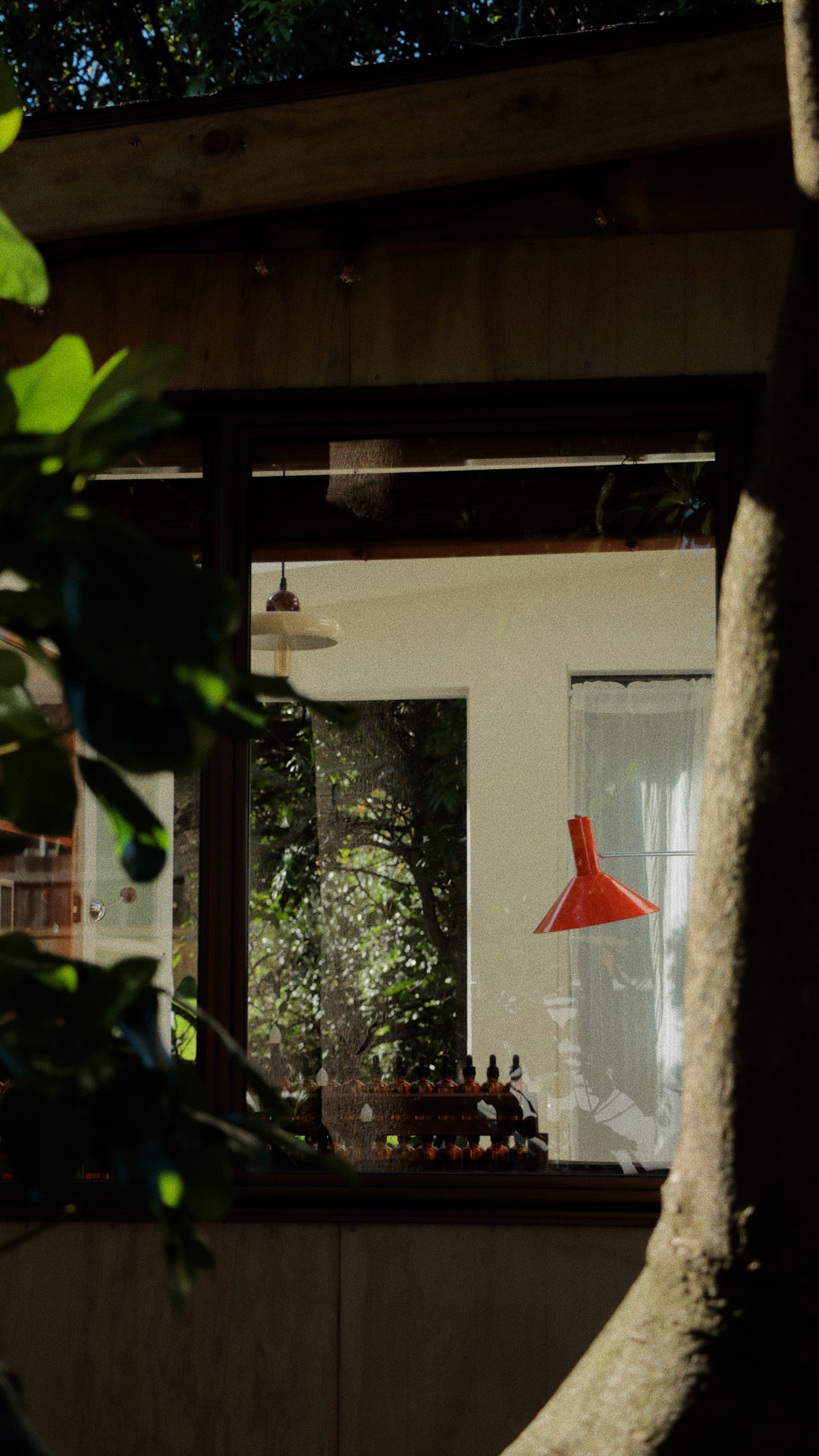 View through the window into a private perfume workshop at SOK Studios in Auckland, featuring scent bottles and a red pendant lamp.