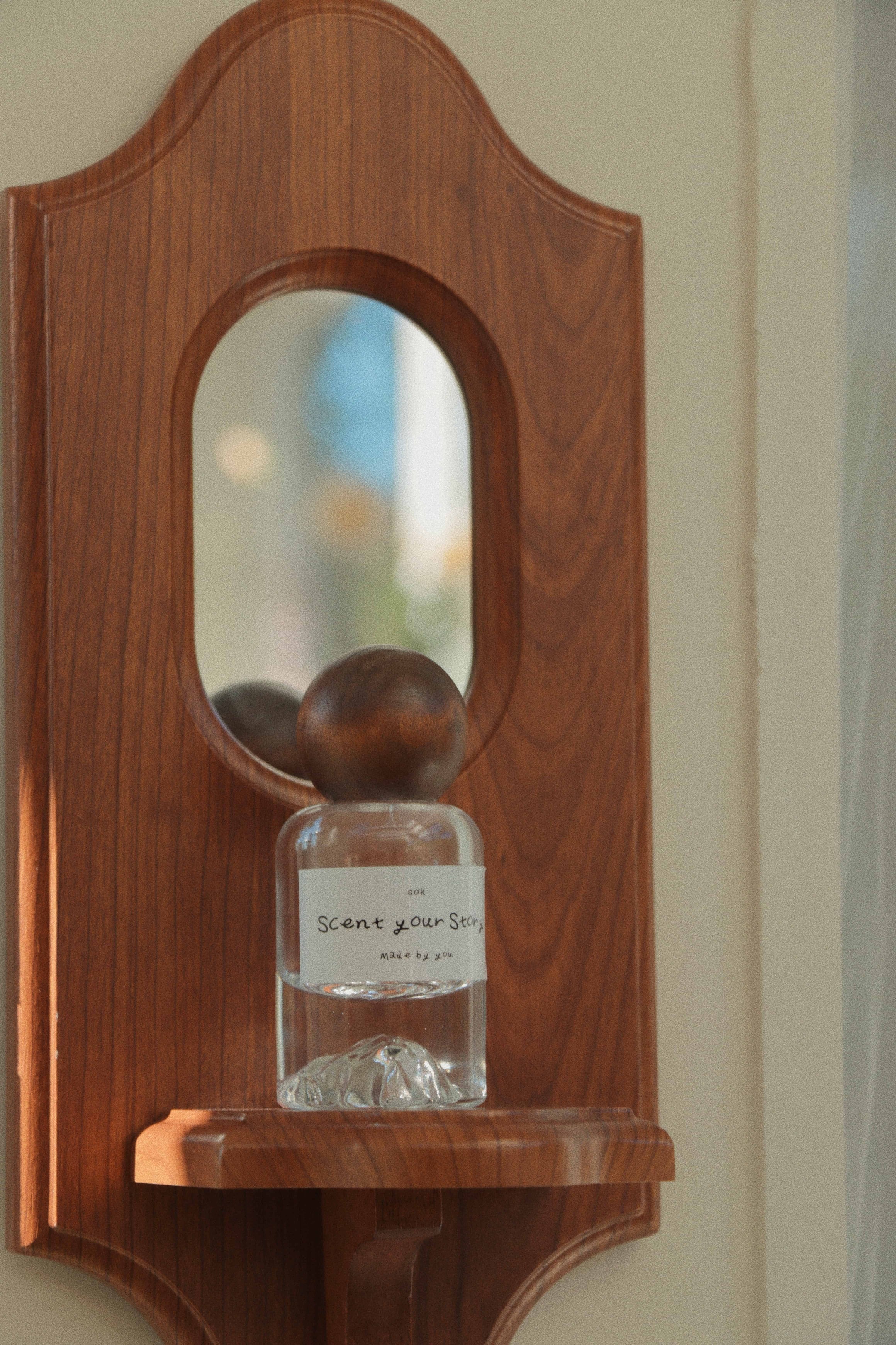 Signature perfume bottle from SOK Studios displayed on a wooden wall shelf, reflecting soft natural light in the studio.