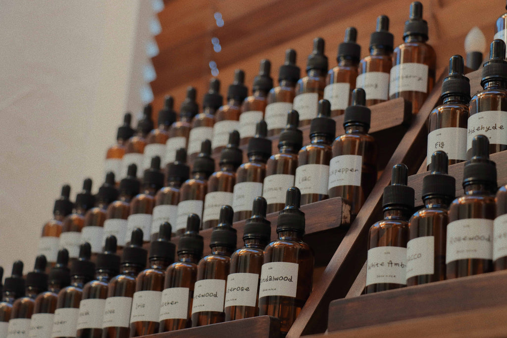 SOK Studios perfume workshop scent library with rows of brown glass dropper bottles labeled with fragrance notes, displayed on a tiered wooden shelf.