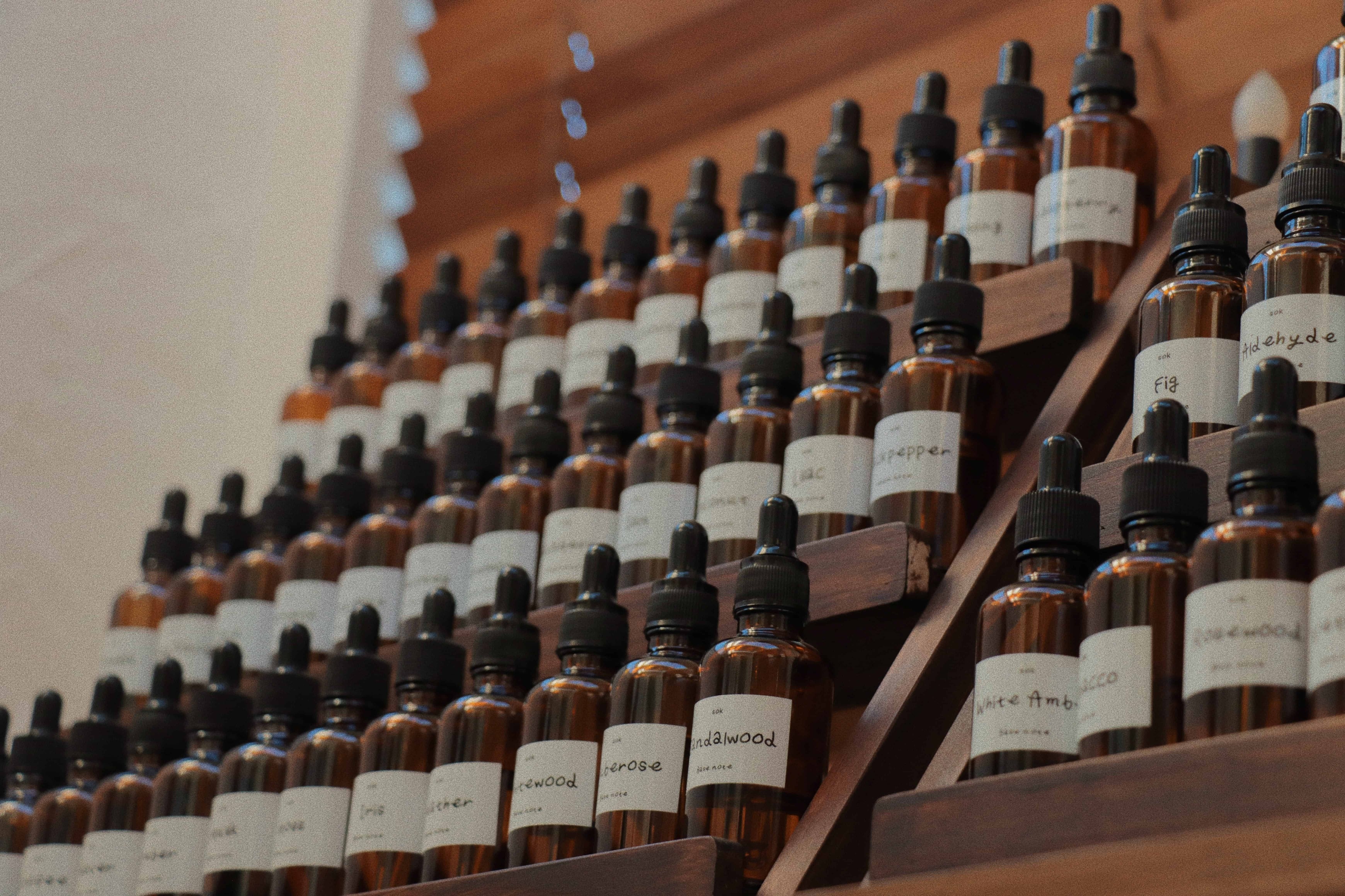 SOK Studios perfume workshop scent library with rows of brown glass dropper bottles labeled with fragrance notes, displayed on a tiered wooden shelf.