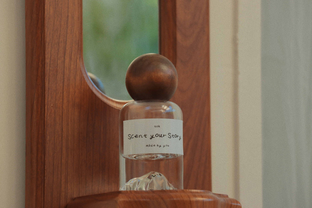 SOK Studios custom perfume bottle labeled 'Scent Your Story' with wooden cap, placed on carved wooden wall shelf inside the perfume workshop